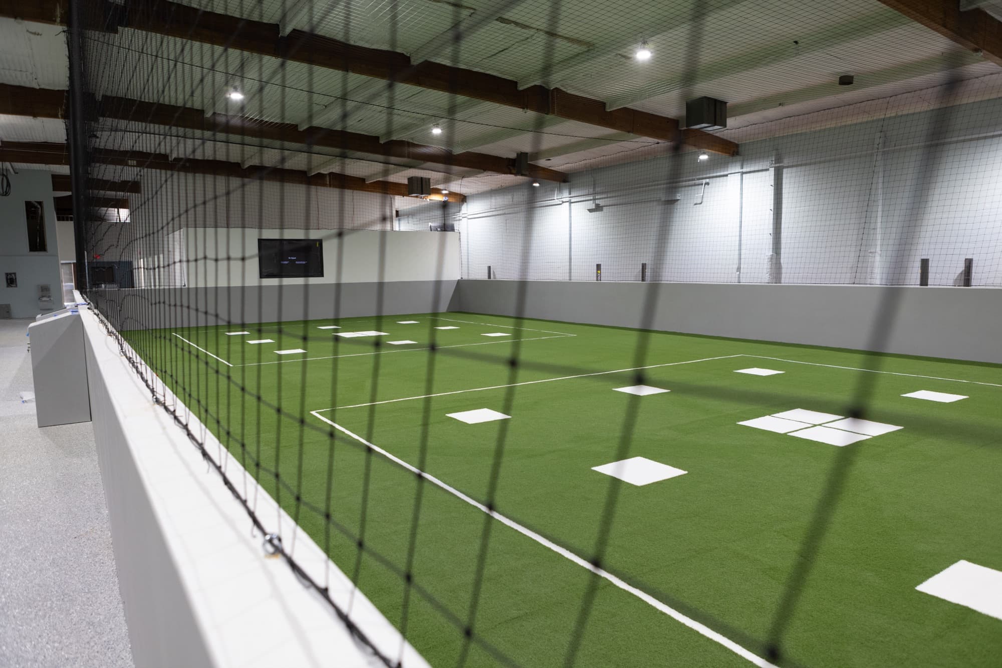 Indoor match-grade turf training lane at Formula Soccer Center, viewed through perimeter netting.